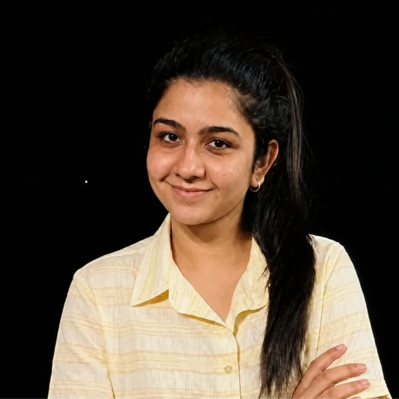 A young woman with long dark hair in a pale yellow shirt smiling softly against a black background